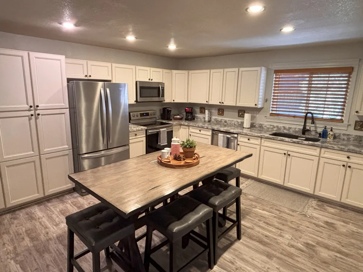 A spacious, open-concept kitchen and dining area is showcased, featuring a large wooden dining table perfect for family meals, modern stainless steel appliances, and ample cabinetry. Natural light streams in through a window, and the atmosphere is warm and welcoming, ideal for cooking together and sharing stories.