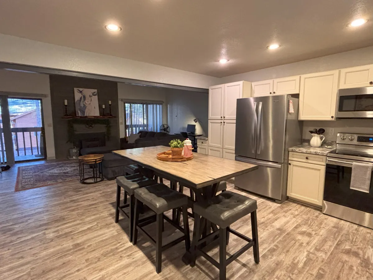 The image showcases a bright, inviting open-concept living area with a modern kitchen featuring a central island and gleaming stainless steel appliances. The spacious room is perfect for gathering, with comfortable seating and tasteful artwork on the wall, creating a warm, welcoming atmosphere ideal for both relaxation and togetherness.