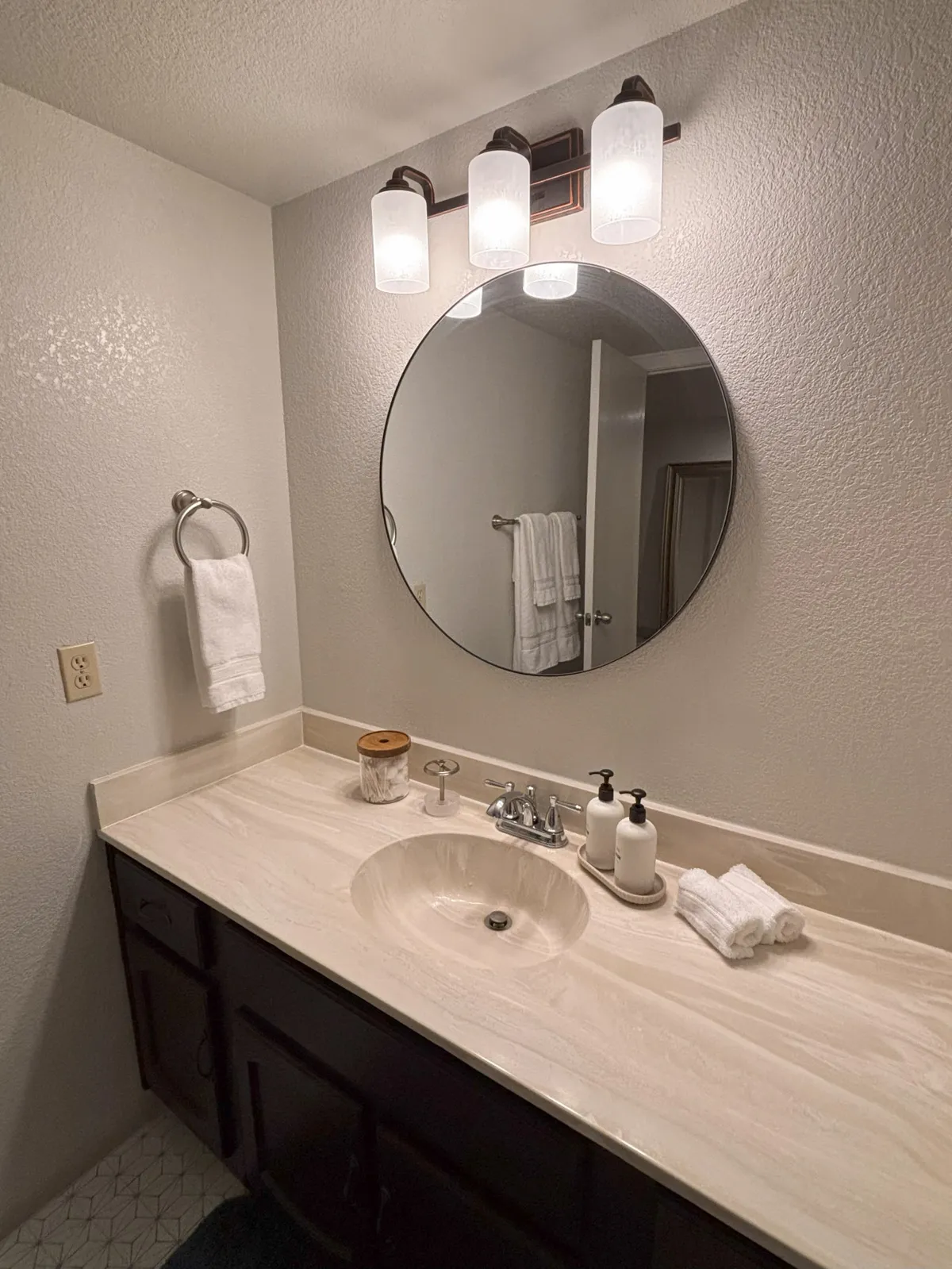 A modern bathroom scene with a mirrored cabinet, stylish light fixtures, a sleek sink, and a spacious vanity countertop. The space feels refreshing and private, ideal for morning and evening routines.