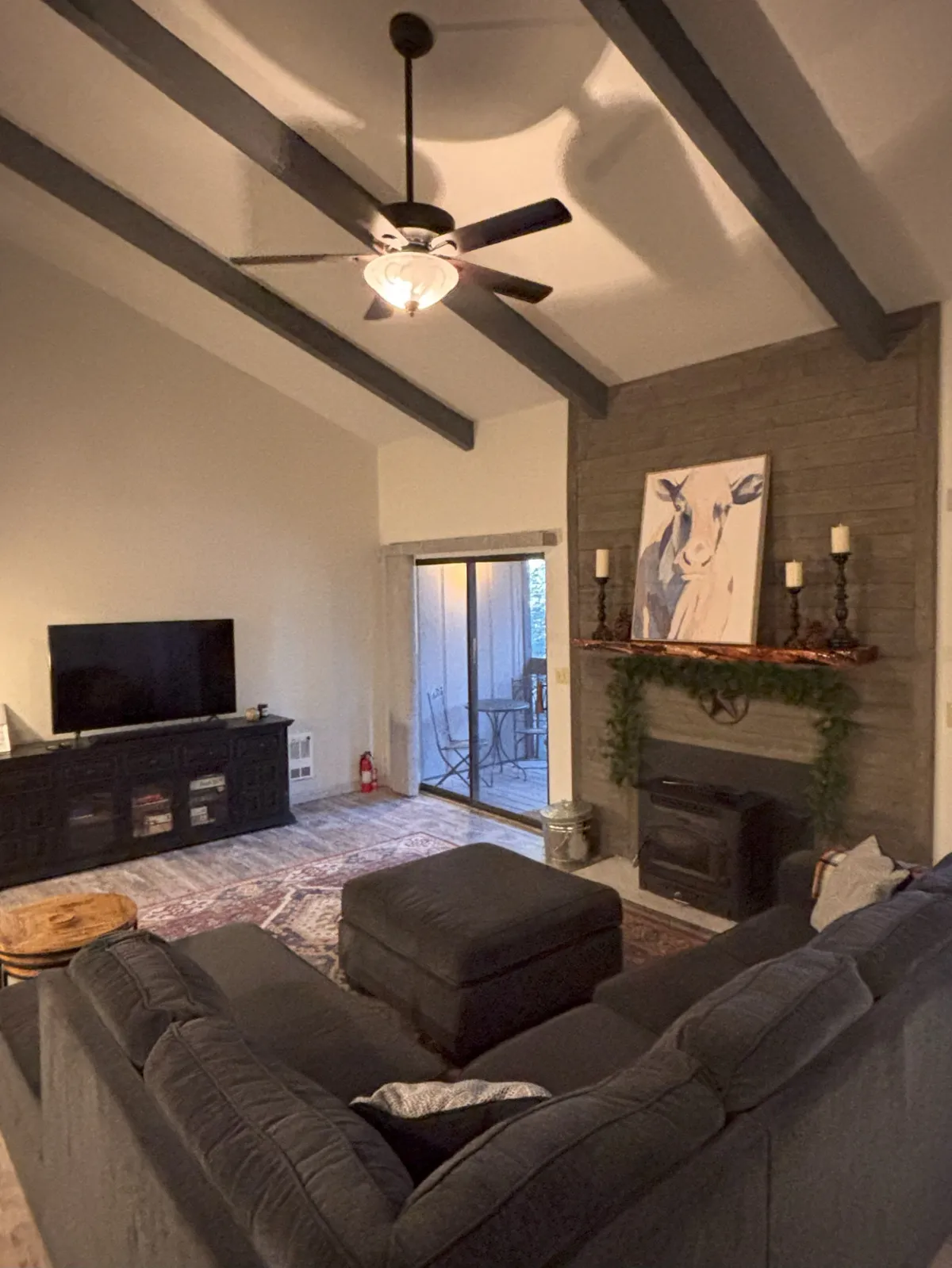 A spacious and warm great room featuring a comfortable sofa, a television, and a fireplace, accented by tasteful artwork on the walls. The open layout and cozy furnishings create an inviting space for gathering and relaxing after outdoor adventures.
